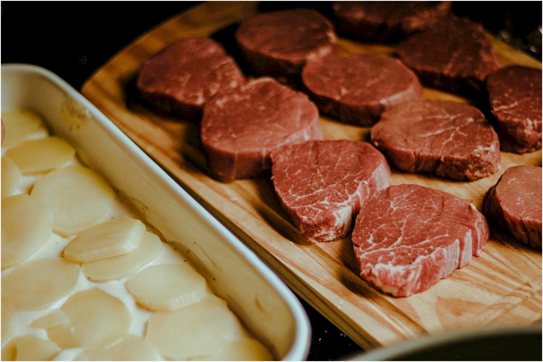 Close-up of uncooked beef steaks and potato slices on a rustic wooden tray, perfect for a gourmet meal.