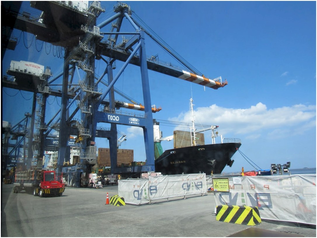 Large cranes at a busy shipping port with cargo containers.