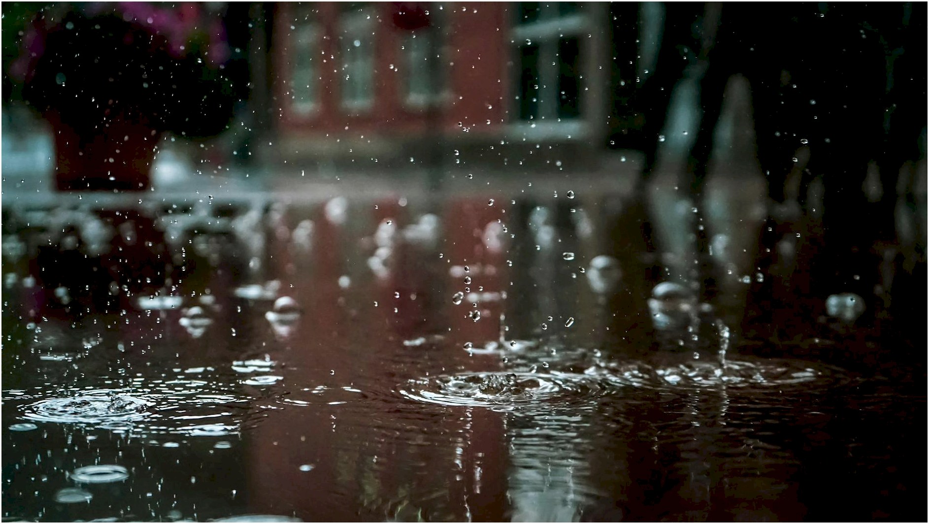Close-up of raindrops splashing into a puddle, capturing reflections and textures in an outdoor urban setting.