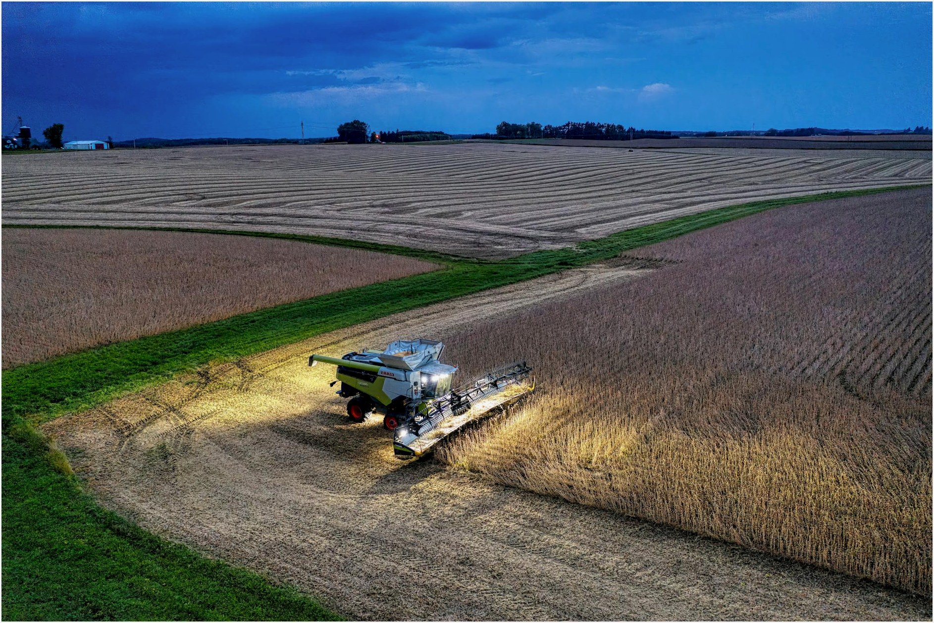 Drone captures a combine harvester working in Minnesota soybean fields at dusk.