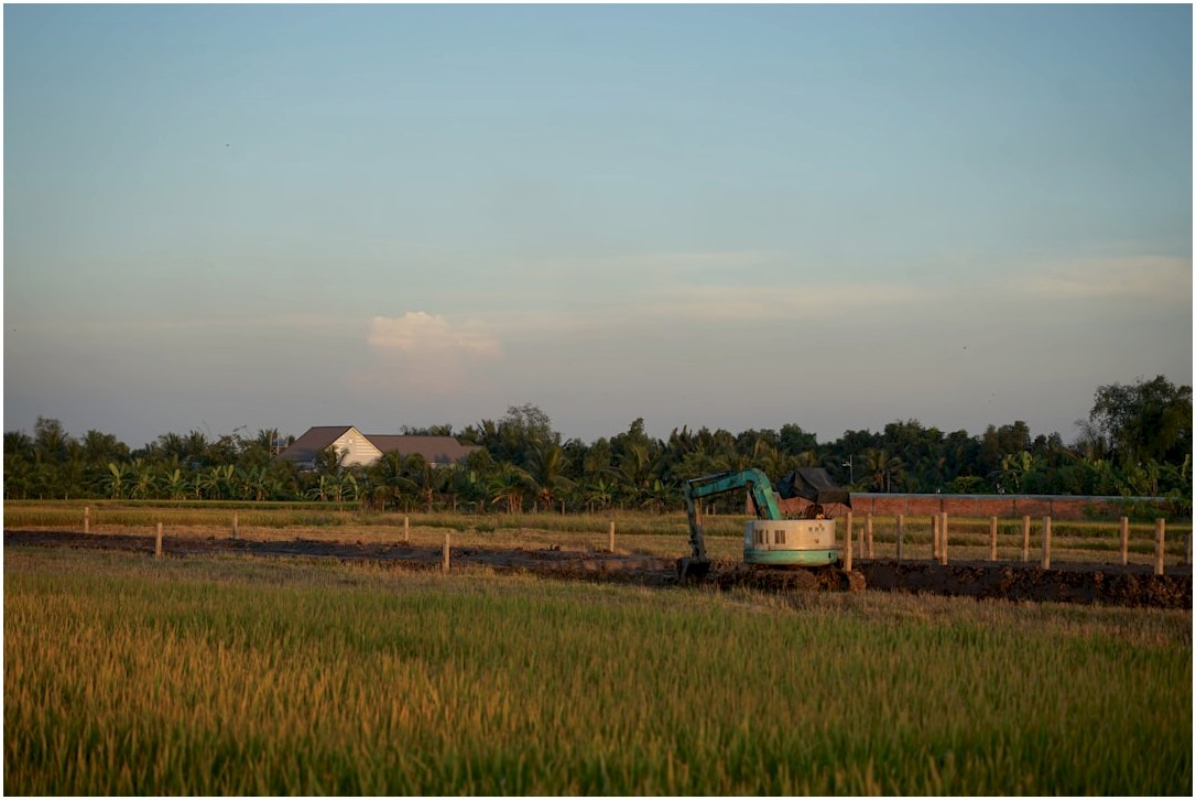 Excavator working in a rural field at sunset.