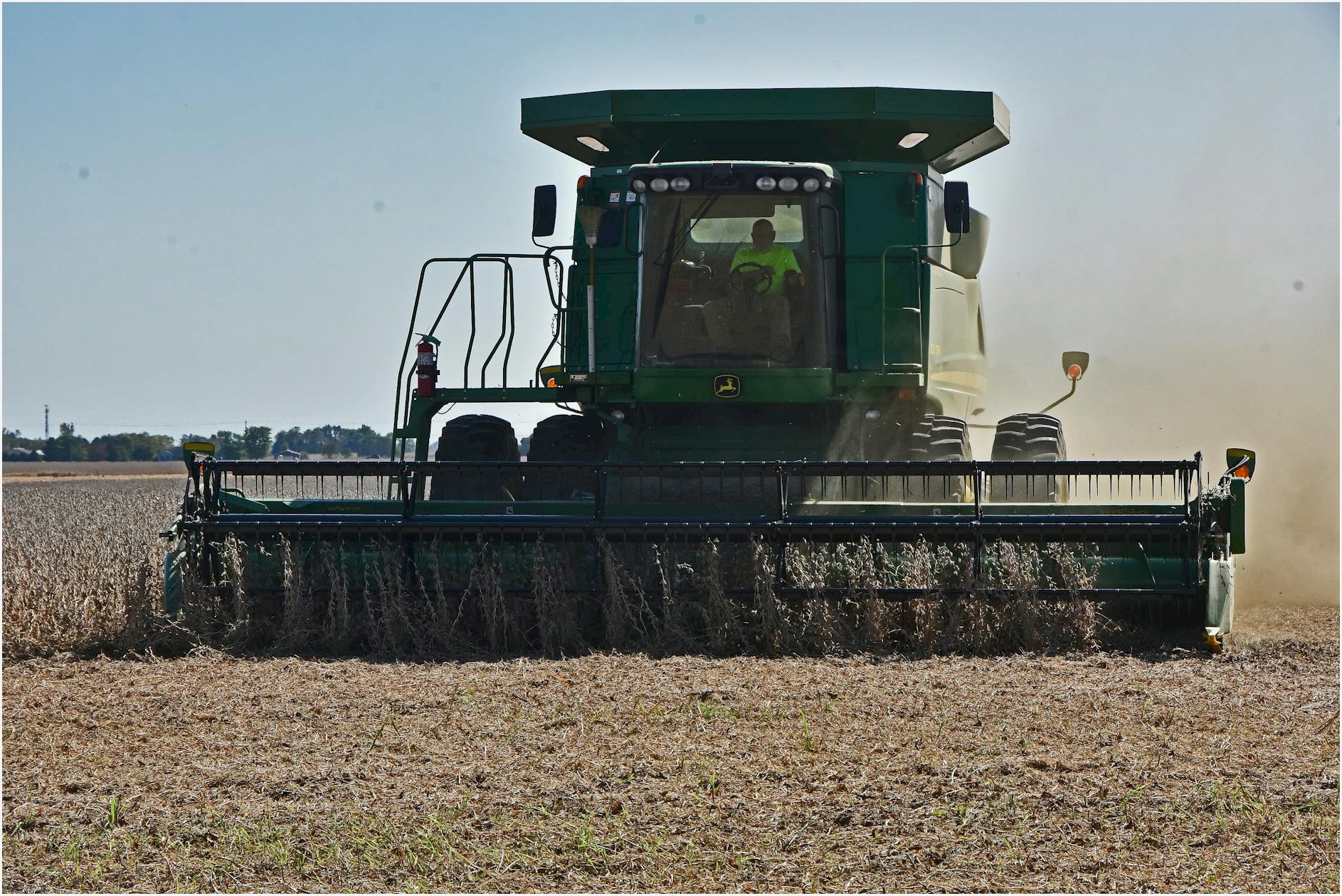 A combine harvester working in a field under clear blue sky during fall harvest.