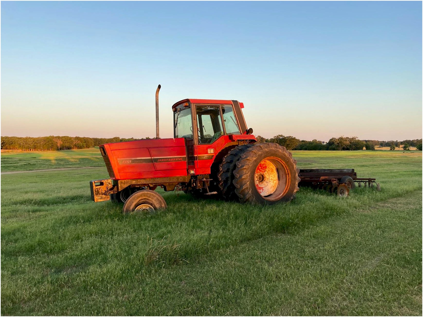 A red tractor parked in a vast green field under a clear sky at sunset.