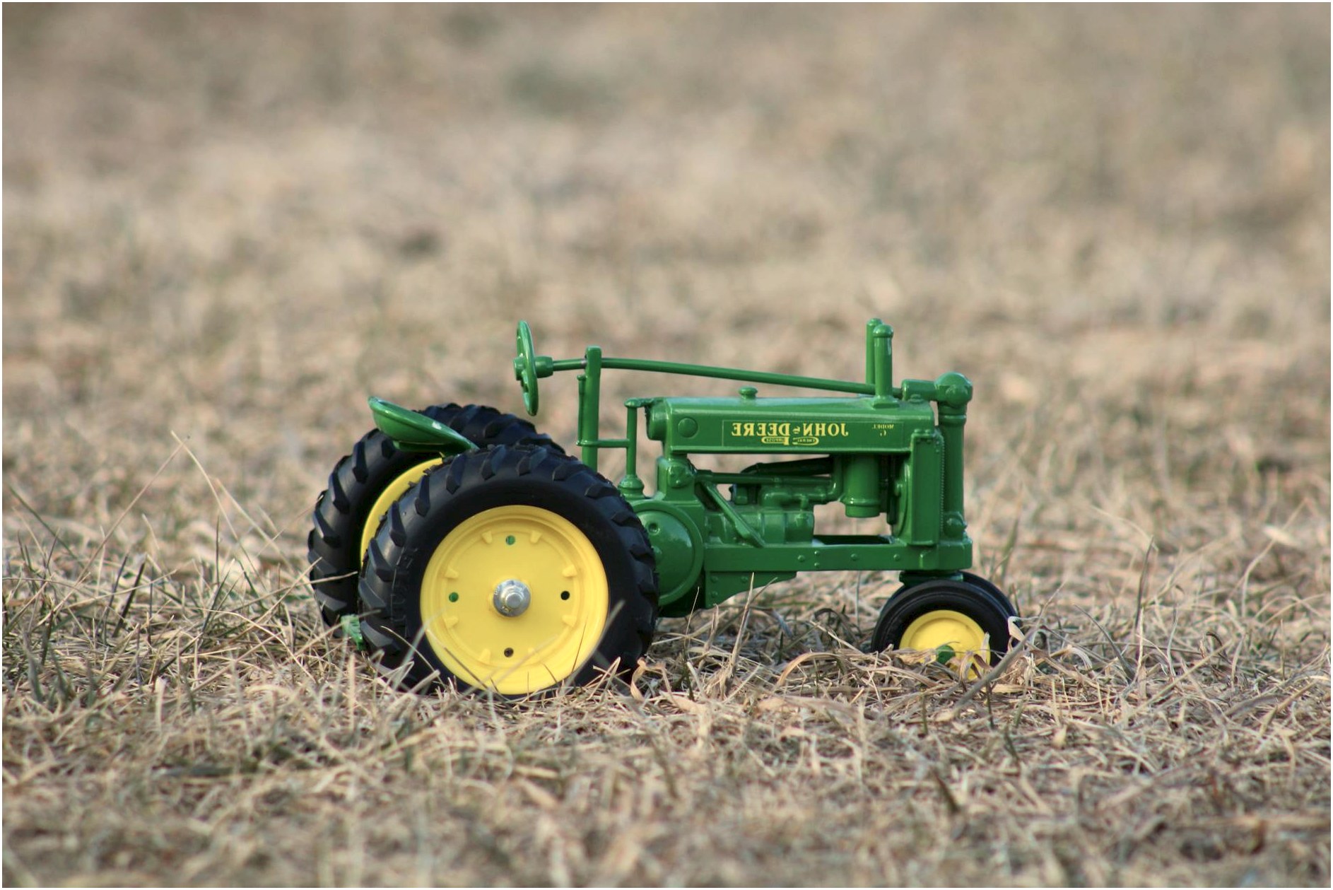 A green toy tractor on a dry field, symbolizing agriculture and rural life.
