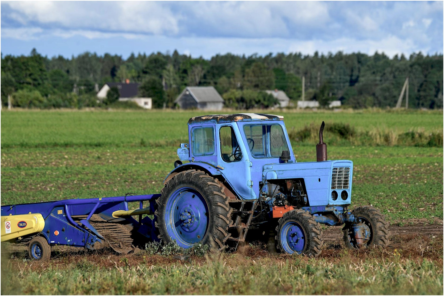 A classic blue tractor working in a lush green field in Harju County, Estonia.