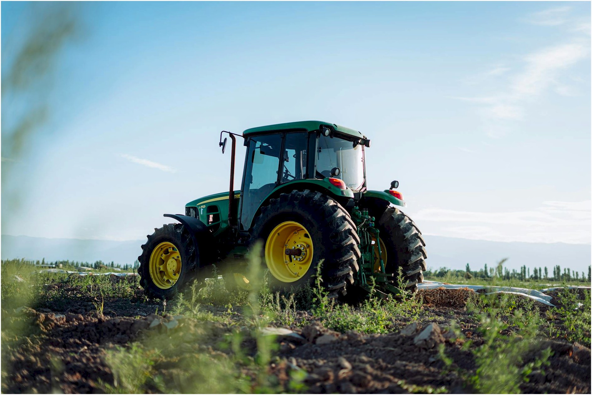 A vibrant green tractor on a farm in Mendoza, Argentina, under clear blue skies.