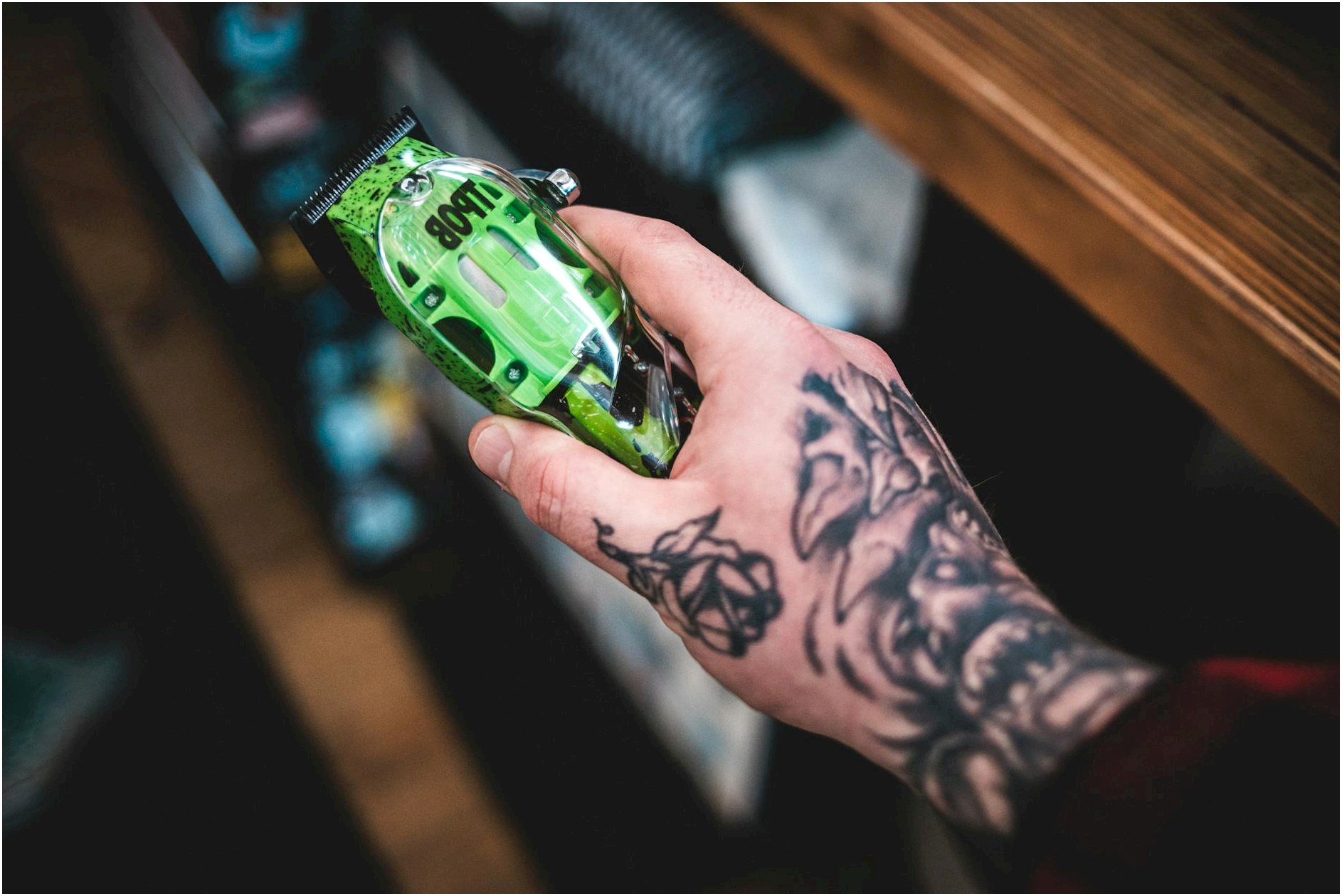 Close-up of a tattooed hand holding a vibrant green electric razor, showcasing intricate tattoos.