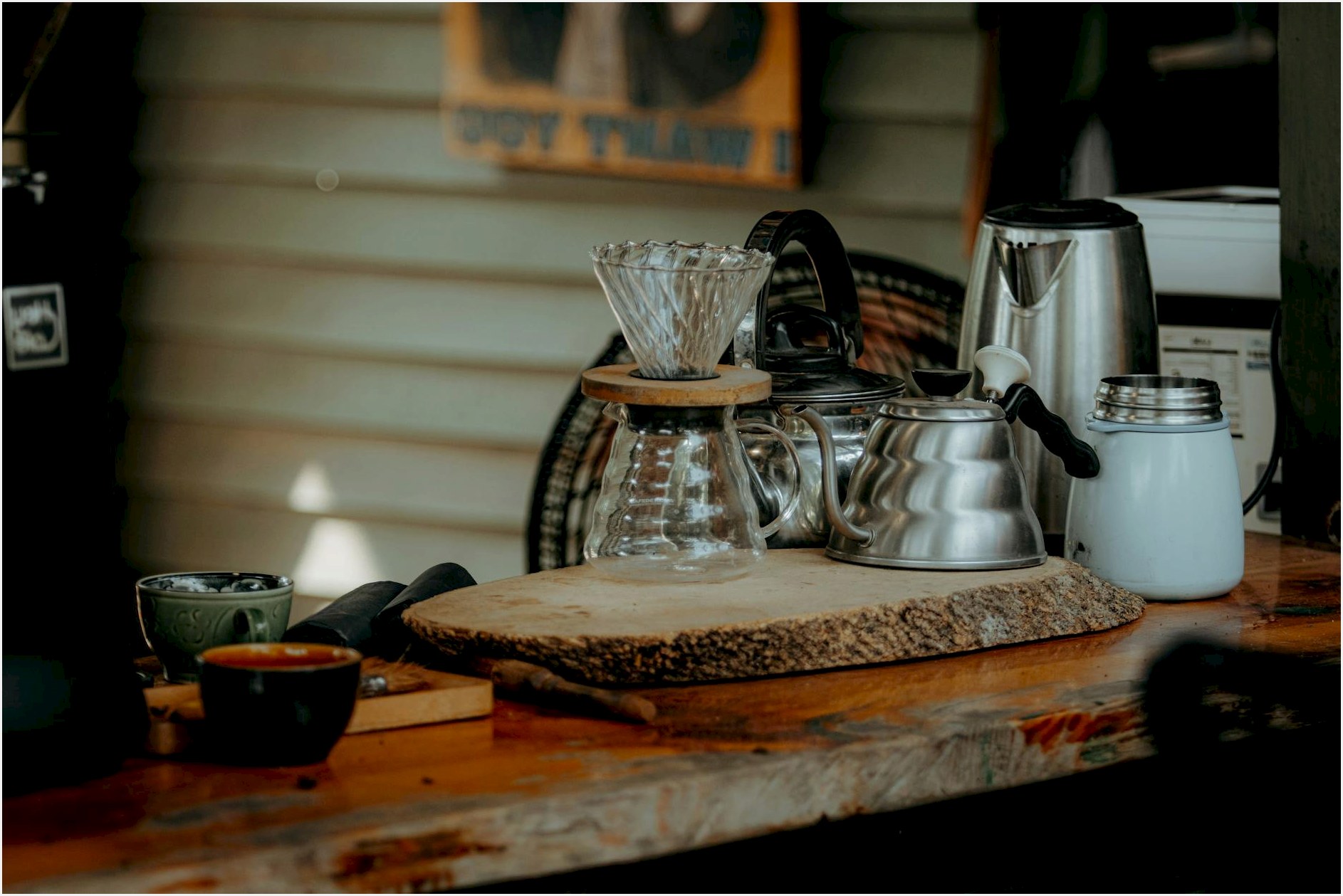 Cozy coffee brewing setup with kettles and cups on a rustic wooden table.