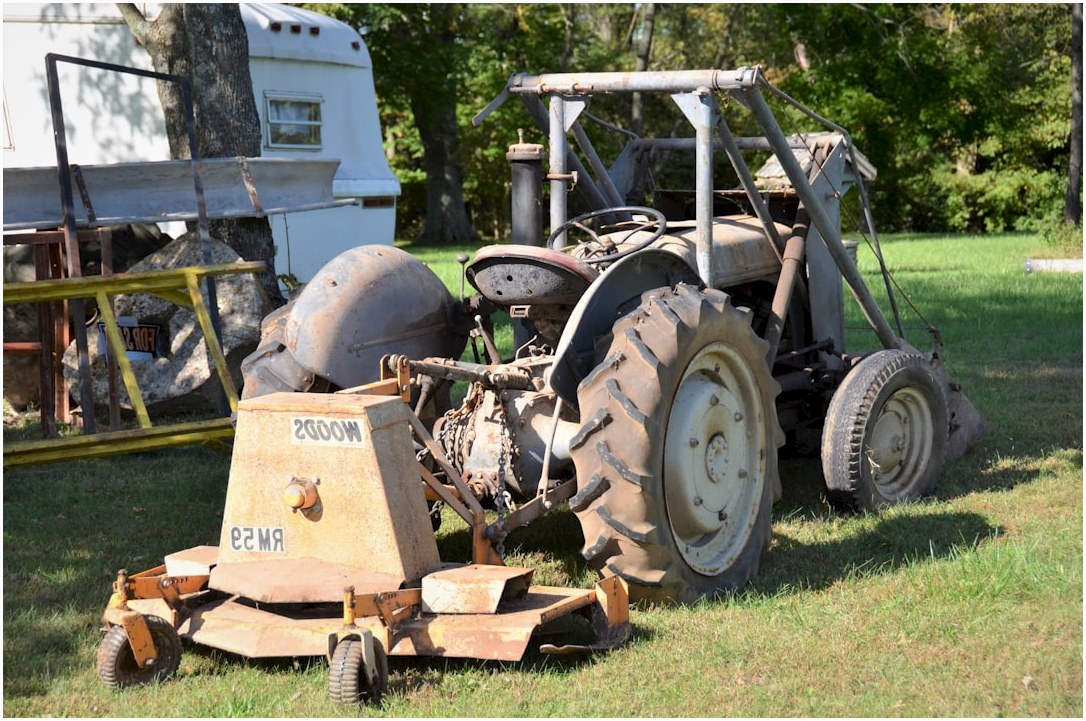 an old tractor sitting in the grass next to a trailer
