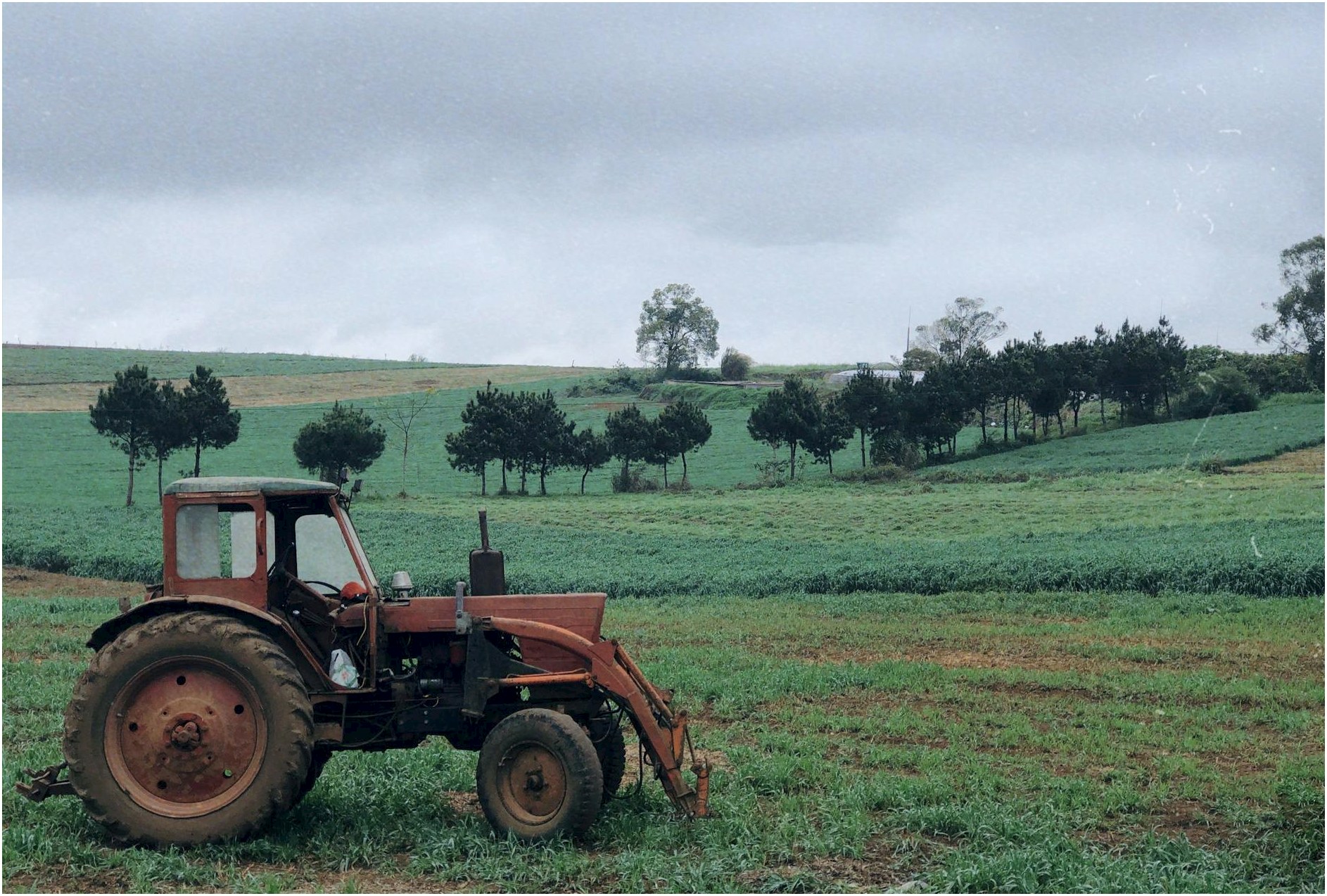 An old tractor sits in a lush green countryside field under a cloudy sky showcasing rural life.