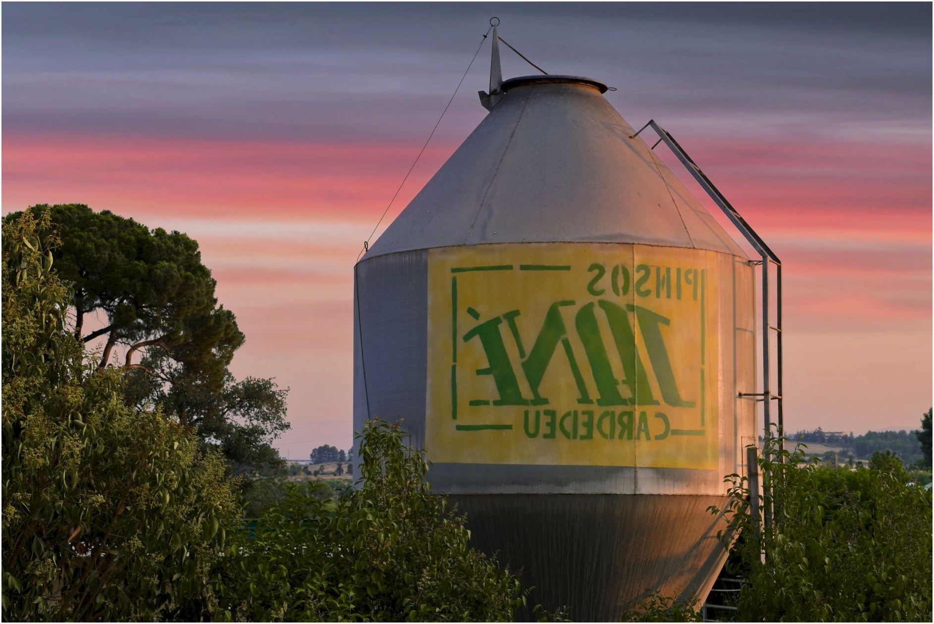 Industrial silo amidst lush greenery in Sant Cugat del Vallès, Spain, at sunset.