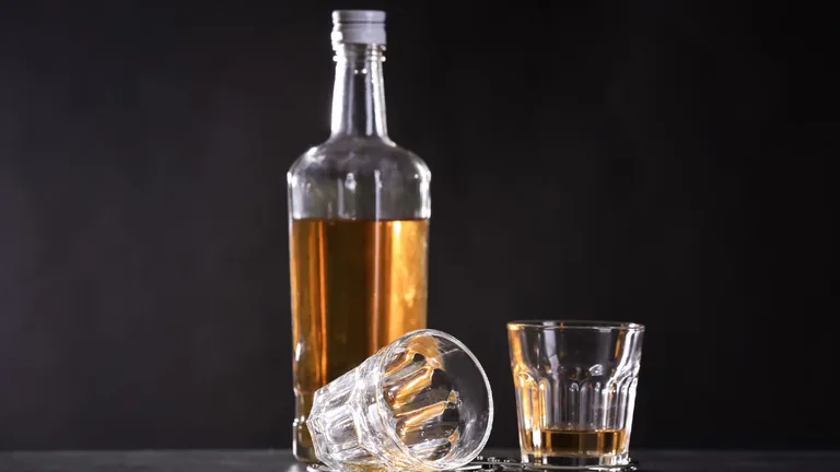 Garrafa de cachaça e copos sobre uma mesa escura
