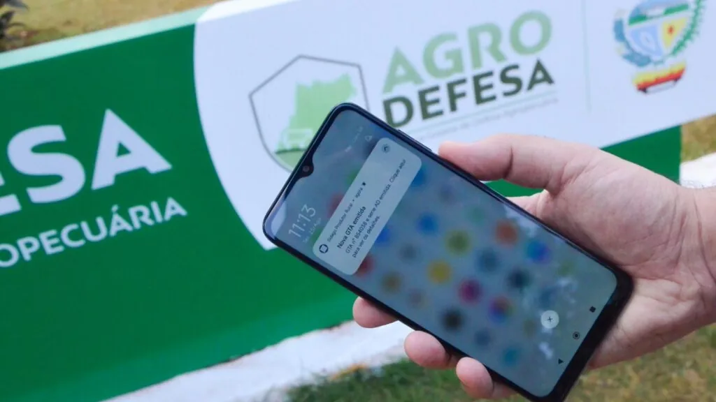 Produtor segura celular com aviso do aplicativo Sidago diante de material da Agrodefesa